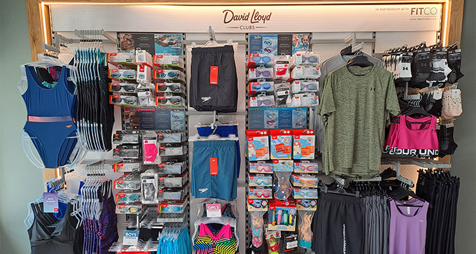 Sportswear display with swimwear, goggles, shorts, and athletic apparel, featuring items from David Lloyd Clubs and Fitco.